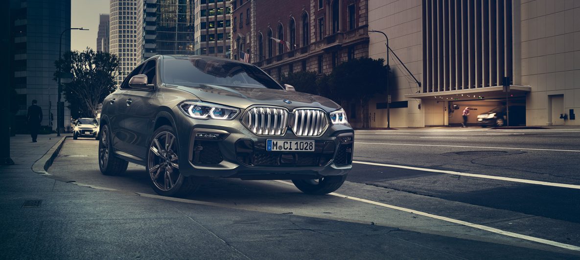 BMW X6 M50i in Dreiviertel-Frontperspektive stehend vor urbaner Kulisse